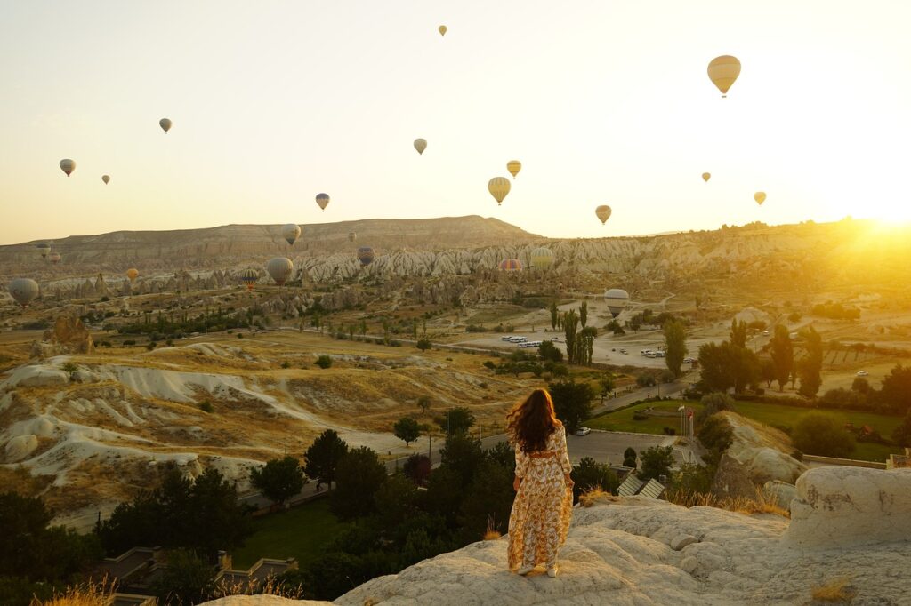 Woman looking over a valley and hot air balloons in the air