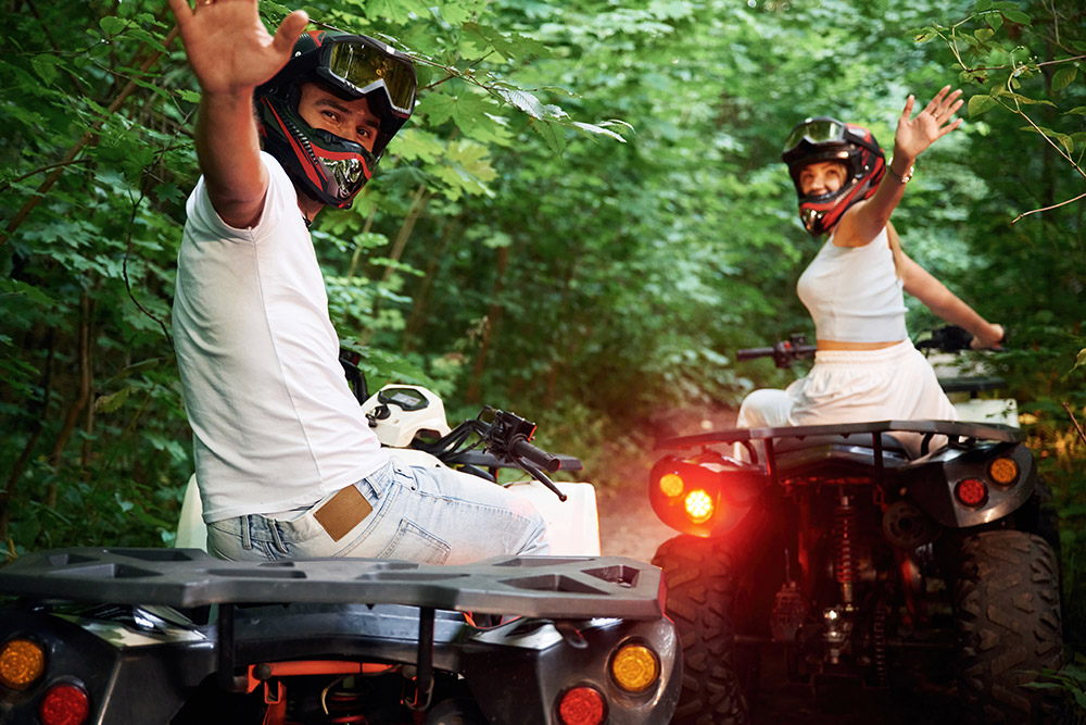 Male and female ATV riders waving