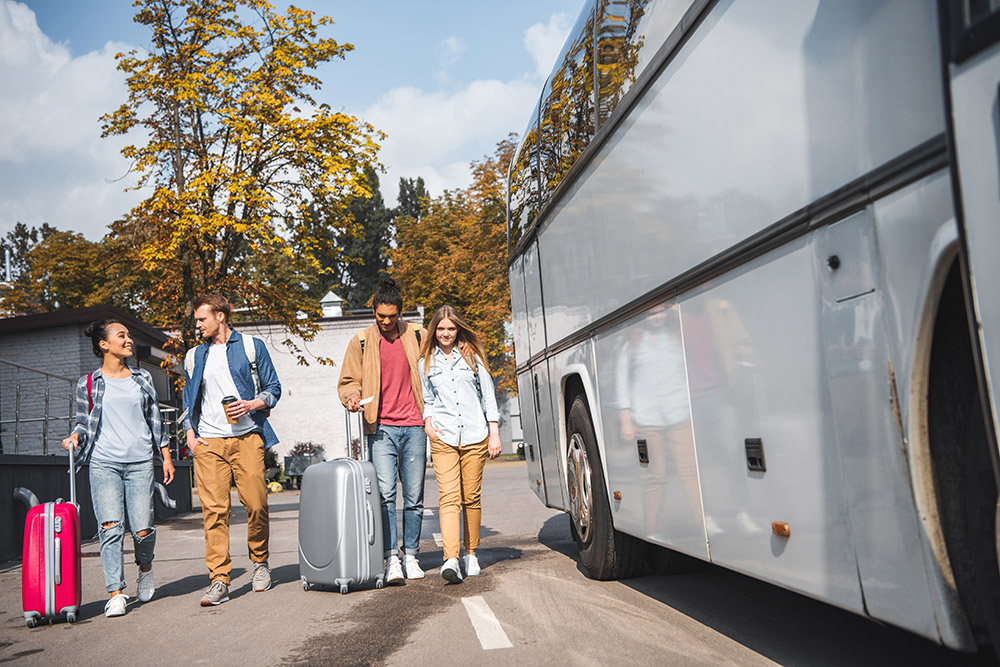 Two young couples with luggage walking by a bus